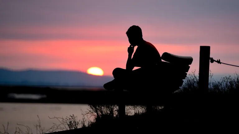 Uma pessoa sentada em um banco vendo o pôr do sol.