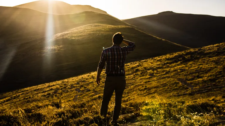 Esta nova vida que vivemos na graça de Deus é demonstrada pelos frutos de obras justas. Então, a graça, a benignidade e amor de Deus para conosco, nos motiva a mudar e ajuda a gerar o desejo de receber a natureza divina, a mente de Deus. Um homem olhando para uma vista de colinas com o sol nos olhos.